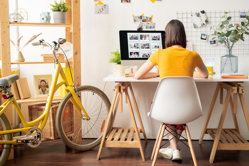 Dame im gelben Oberteil sitzt im Home Office an ihrem Schreibtisch.